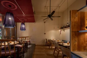 A minimalist restaurant interior with wooden tables, fabric lampshades, and wood paneling.