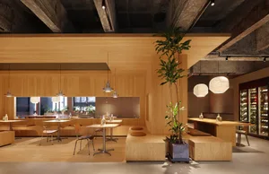 A modern restaurant interior with wooden walls, tables, and seating areas, featuring plants and hanging lantern-style lights.