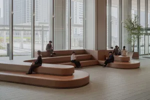 People working in a minimalist office space with wooden seating and large windows.