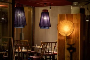 A cozy restaurant interior with wooden tables, fabric shades, and glass chandeliers.