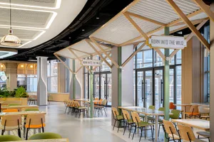 A minimalist cafeteria interior with light-colored wooden furniture, open-air design, and modern signage.