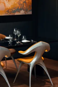 A sleek, modern dining area featuring metallic chairs with orange seats and a dark table, complemented by elegant glassware a