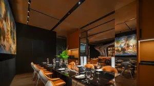 Modern, metallic-finished restaurant interior with black tables and orange chairs in a minimalist design.
