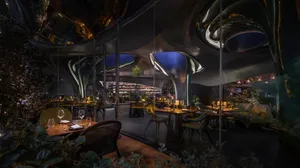 Modern restaurant interior featuring metallic structures, glass walls, and greenery