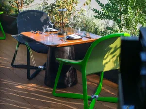 A stylish restaurant setting with a wooden table and green chairs surrounded by plants.