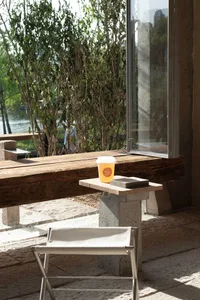 A modern coffee shop exterior with wooden seating and concrete structures, surrounded by greenery, with a cup of drink on a s