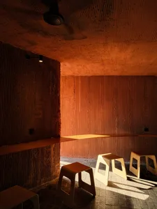 A cozy cafe interior featuring textured concrete walls and minimalist wooden stools.