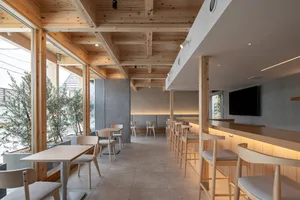 A minimalist coffee shop with wooden tables and chairs, concrete walls, and natural light.