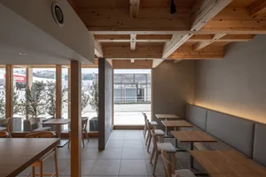 Modern cafe interior with wooden tables, chairs, and exposed wooden beams.