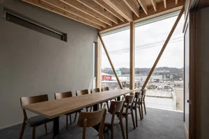 Modern conference room featuring a wooden table and chairs, with a large window providing natural light and a cityscape view.