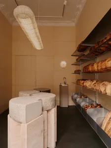 A minimalist bakery interior with wooden shelves, concrete blocks, and metal racks.