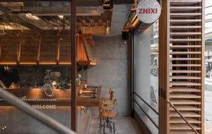 Modern cafe interior featuring a wooden bar counter with stools, industrial lighting fixtures, and a sign displaying 'ZHIXI'.