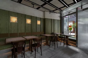 Industrial restaurant interior with green wooden walls, wooden tables, and chairs.