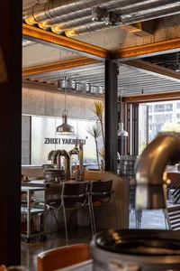 Industrial-style restaurant interior with exposed metal beams, concrete walls, and glass elements.