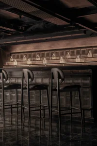 Industrial-style bar with metal stools and a backlit shelf displaying decanters.