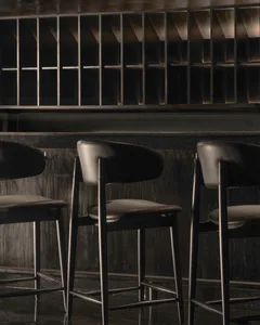 A modern bar featuring sleek metal stools with leather seating against a dark wooden backdrop.