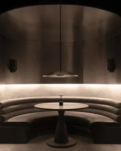Circular dining table and bench seating in a minimalist restaurant setting with leather cushions, concrete flooring, and indu