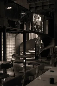 A modern restaurant interior with dark metallic elements and reflective surfaces, featuring tables, chairs, and a spiral stai