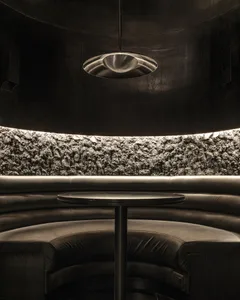 Circular booth with black cushions and a textured, illuminated concrete backdrop in a restaurant setting