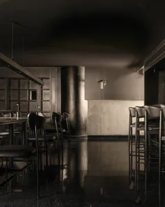 A minimalist, industrial-style restaurant bar with metallic surfaces and black furniture.