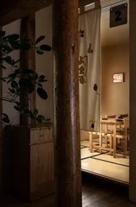 A wooden restaurant interior with a tatami floor, traditional seating, and a hanging curtain with Japanese characters.
