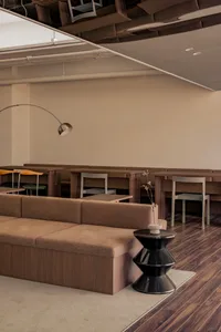 A modern cafe interior with brown wooden tables, chairs, and benches, featuring a black side table with a small vase and a mi