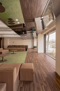 Modern office lounge area with wooden flooring, seating, and green wall.