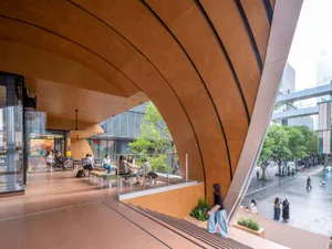 People are seating in a modern public space with a curved architectural design made of sandstone.