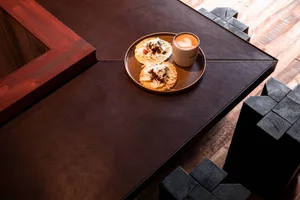 Plate of tacos and coffee cup on a wooden and leather table in a cafe setting.