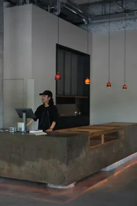 A receptionist in a minimalist industrial lobby with a concrete reception desk and wood accents.