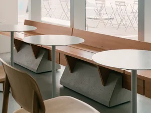 Modern cafe interior with white tables, wooden benches, and concrete base.