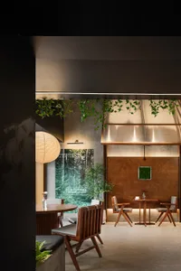 Restaurant interior with wooden furniture, concrete walls, and greenery