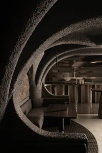 Dark, textured concrete interior design with curved walls and a cozy seating area.