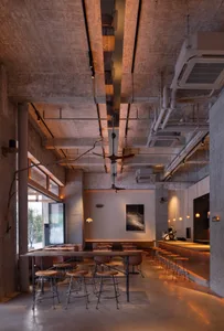 Industrial-style cafe interior with concrete walls, ceiling fans, and wooden stools.