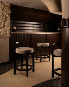 A modern bar counter featuring a wine rack and upholstered stools near a stone wall.