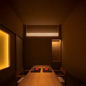 A modern restaurant dining room illuminated by warm, ambient lighting, featuring wooden furniture and minimalist decor.