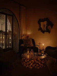 A cozy living room with a mosaic tile table topped with decor items, including a hookah and a bottle of alcohol, surrounded b