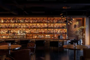 A modern bar interior featuring a wooden counter, metallic furniture, and concrete flooring.