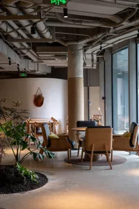 A modern cafe lounge featuring wooden chairs, concrete flooring, and a minimalist design.