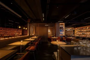 Modern restaurant bar with wooden accents, glass shelves, and stainless-steel countertops.