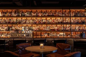 Industrial-style restaurant bar with wooden seating, metal tables, and glass bottles in the background.