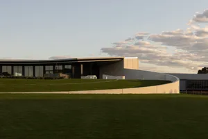 A modern architectural building with concrete exterior and green lawn against a blue sky with clouds.