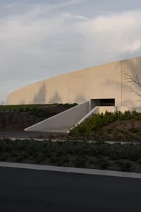 A modern building with a concrete exterior features a sloping alleyway leading up to its entrance.