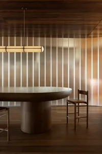 A modern dining room featuring a round wooden table with a fiber-glass table top, accompanied by wooden chairs with leather s