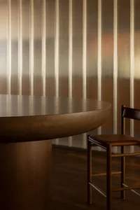 Modern restaurant interior with a wooden table and chair against a metallic striped wall.