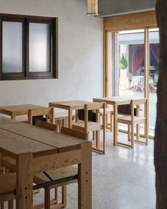 A minimalist restaurant interior with wooden tables and chairs.
