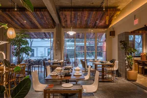 Interior view of a cafe with wooden tables, concrete walls, and indoor plants.