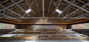 An industrial-style interior with exposed brick walls, wooden benches, and a high, pitched roof with skylights.