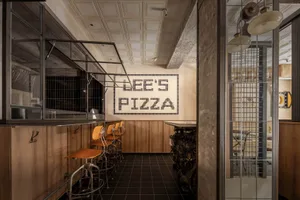 Industrial-themed pizza shop interior with brick walls, concrete columns, and tiled floors.