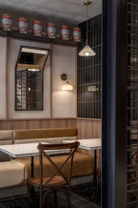 Industrial-style restaurant interior with black tiled walls, concrete flooring, and wooden furniture, featuring a booth seati